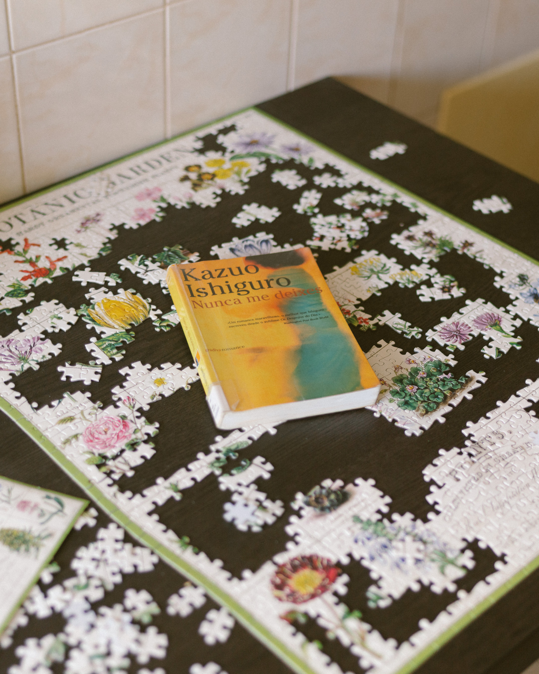 Auto-generated description: A partially completed floral puzzle is spread out on a table with a book titled Kazuo Ishiguro: Nunca me Dejes placed on top.