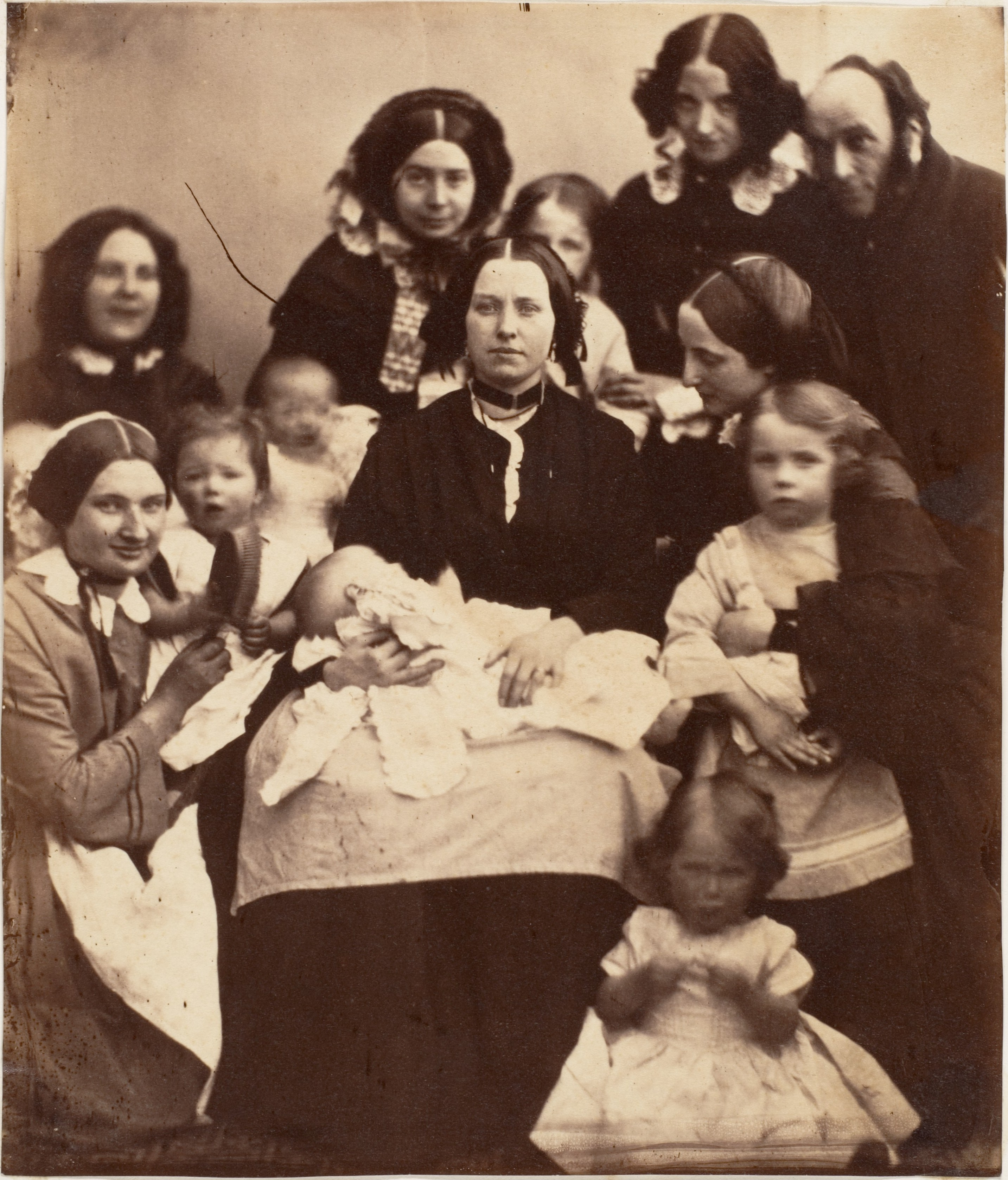 Auto-generated description: A group of adults, mainly women, and children are gathered together, some holding babies, in a vintage-style photograph.